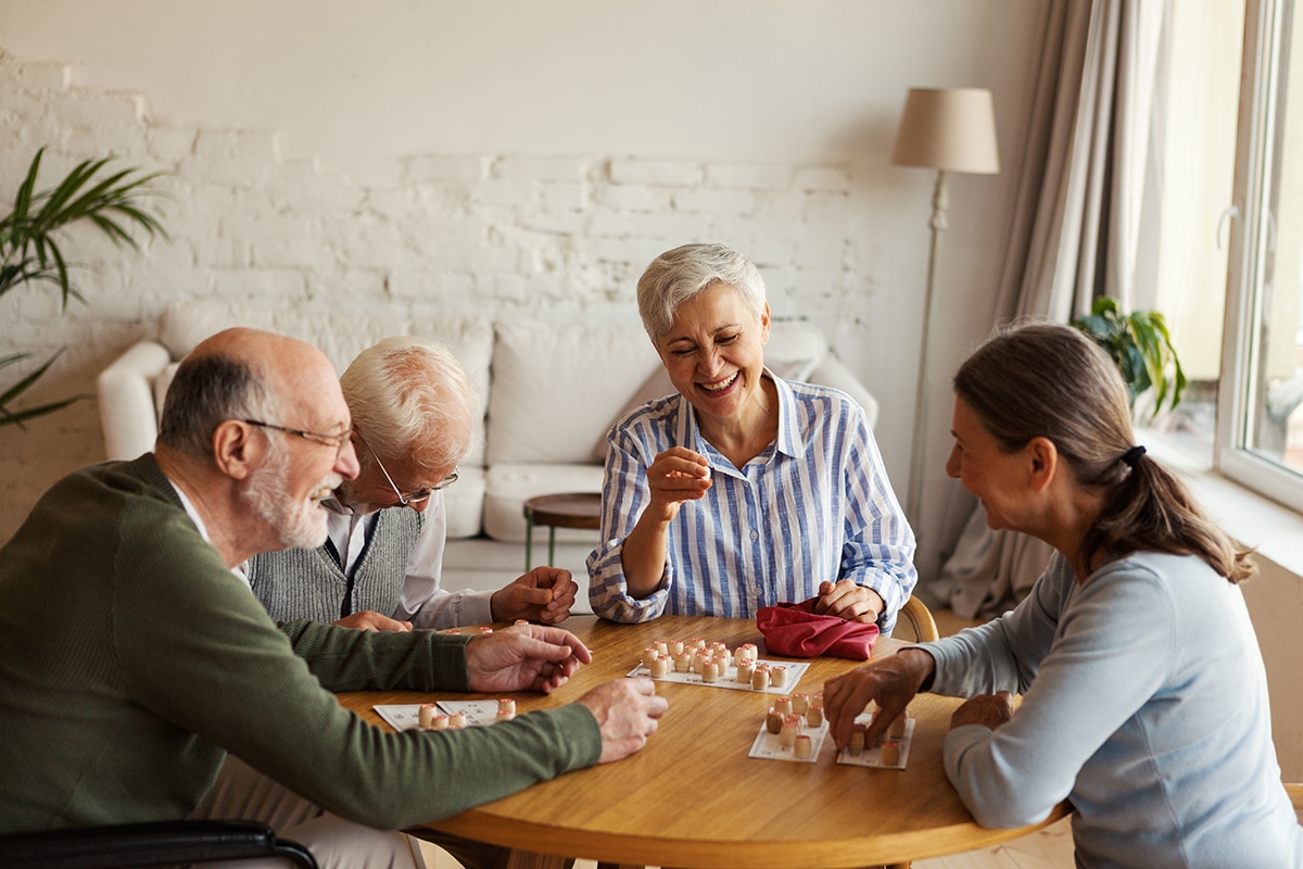 PACS-300x200-activity2 Group of four cheerful senior people, two men and two women, having fun sitting at table and playing bingo game in nursing home