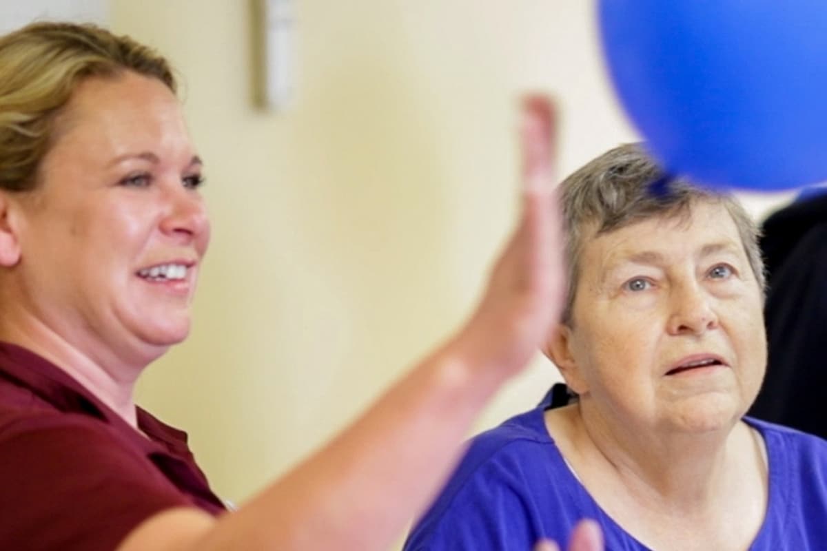 Team member assisting an older woman with a group activity