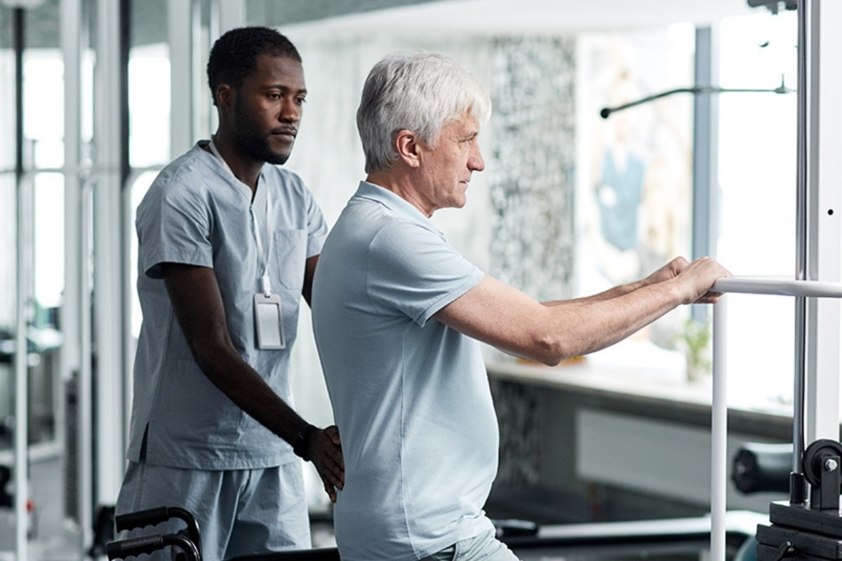 Care professional assisting an older man with mobility exercises in a rehabilitation setting