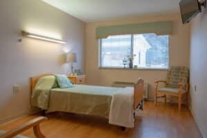 Private resident room with a bed, window, chair and bedside table at Prairie Heights