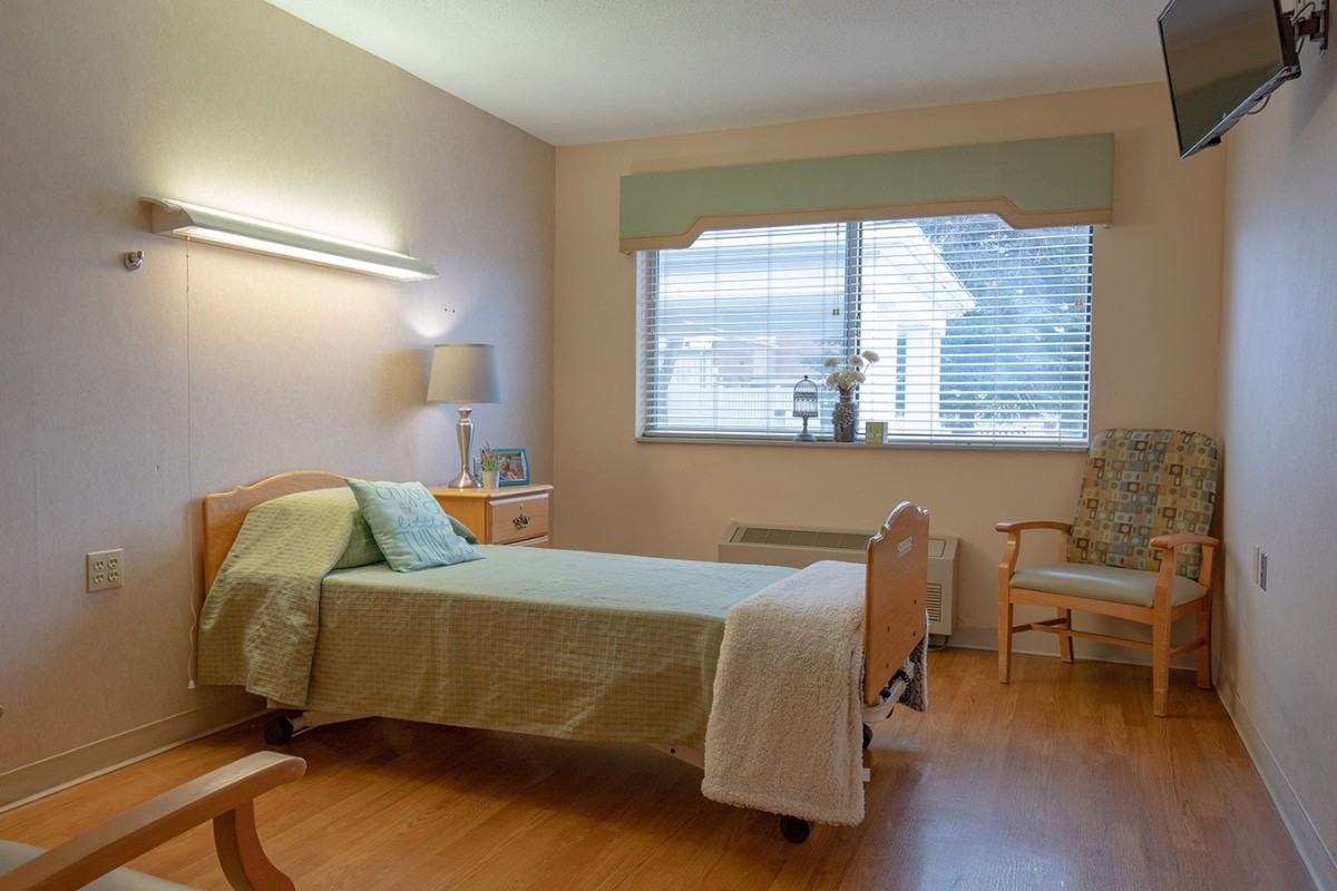 Private resident room with a bed, window, chair and bedside table at Prairie Heights
